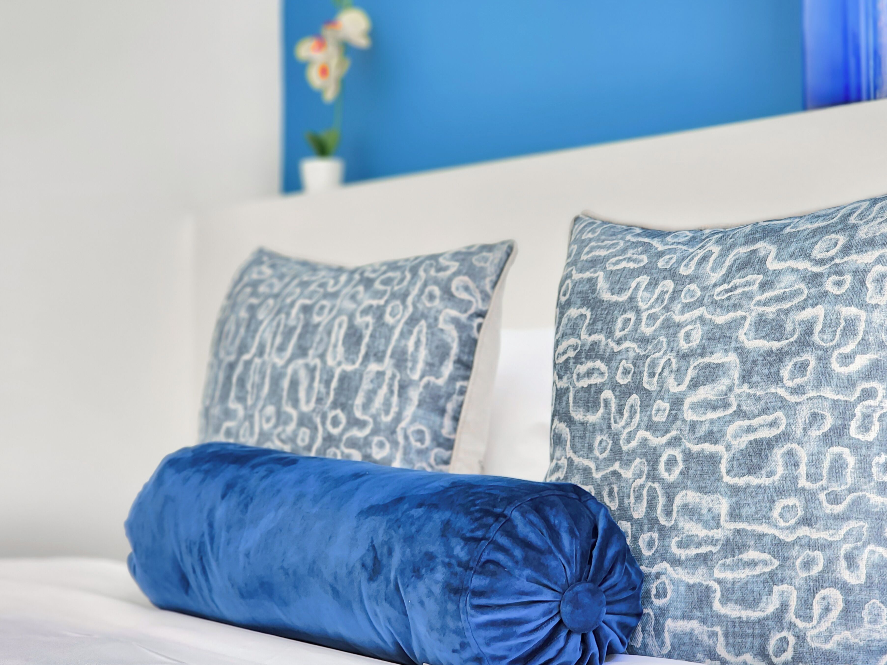 A bed with two patterned pillows and a solid blue pillow.