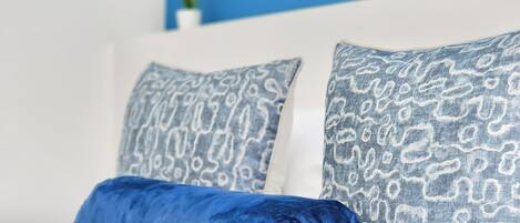 A bed with two patterned pillows and a solid blue pillow.