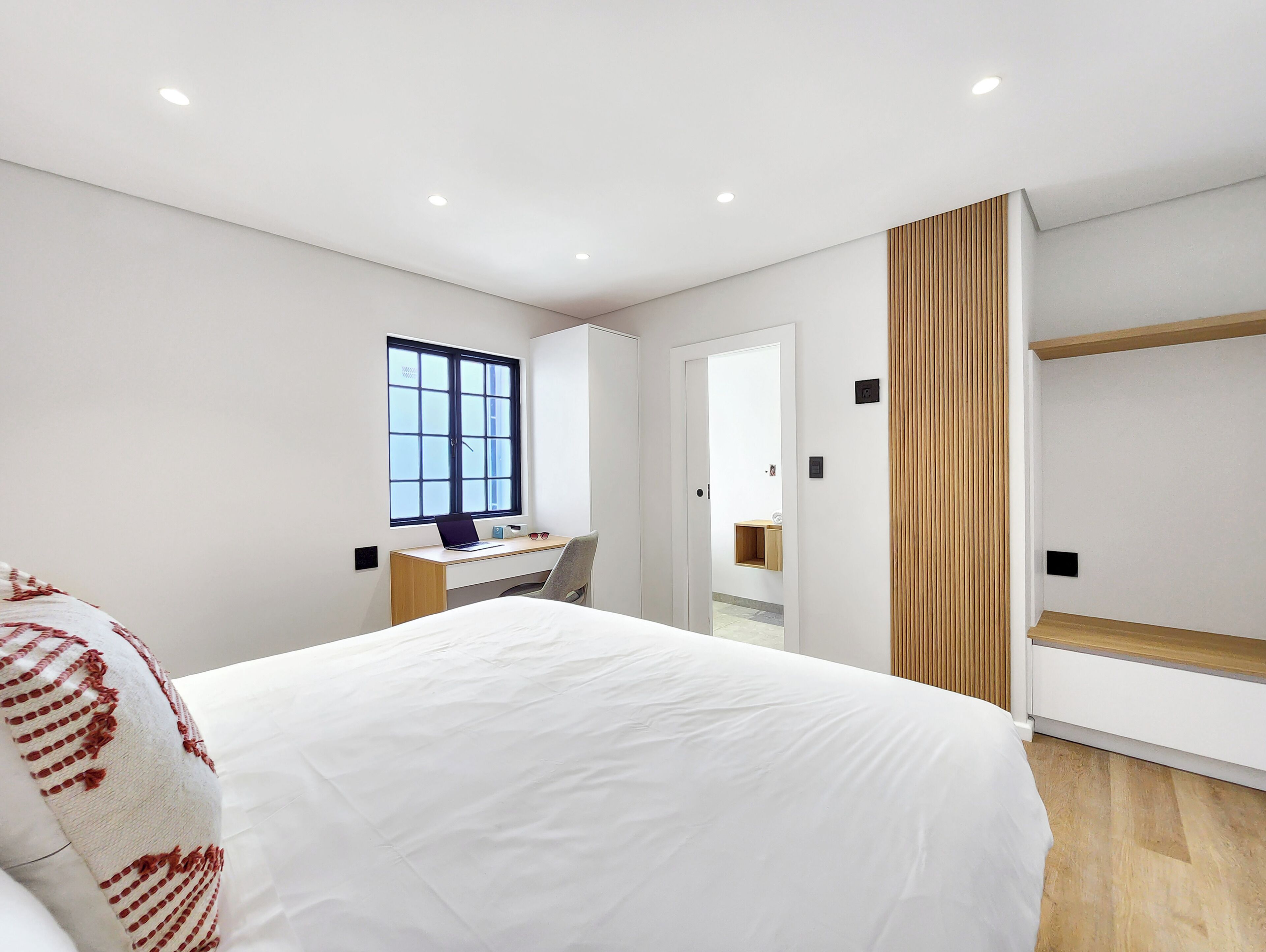 A modern bedroom with a large bed, a desk, and a wardrobe.