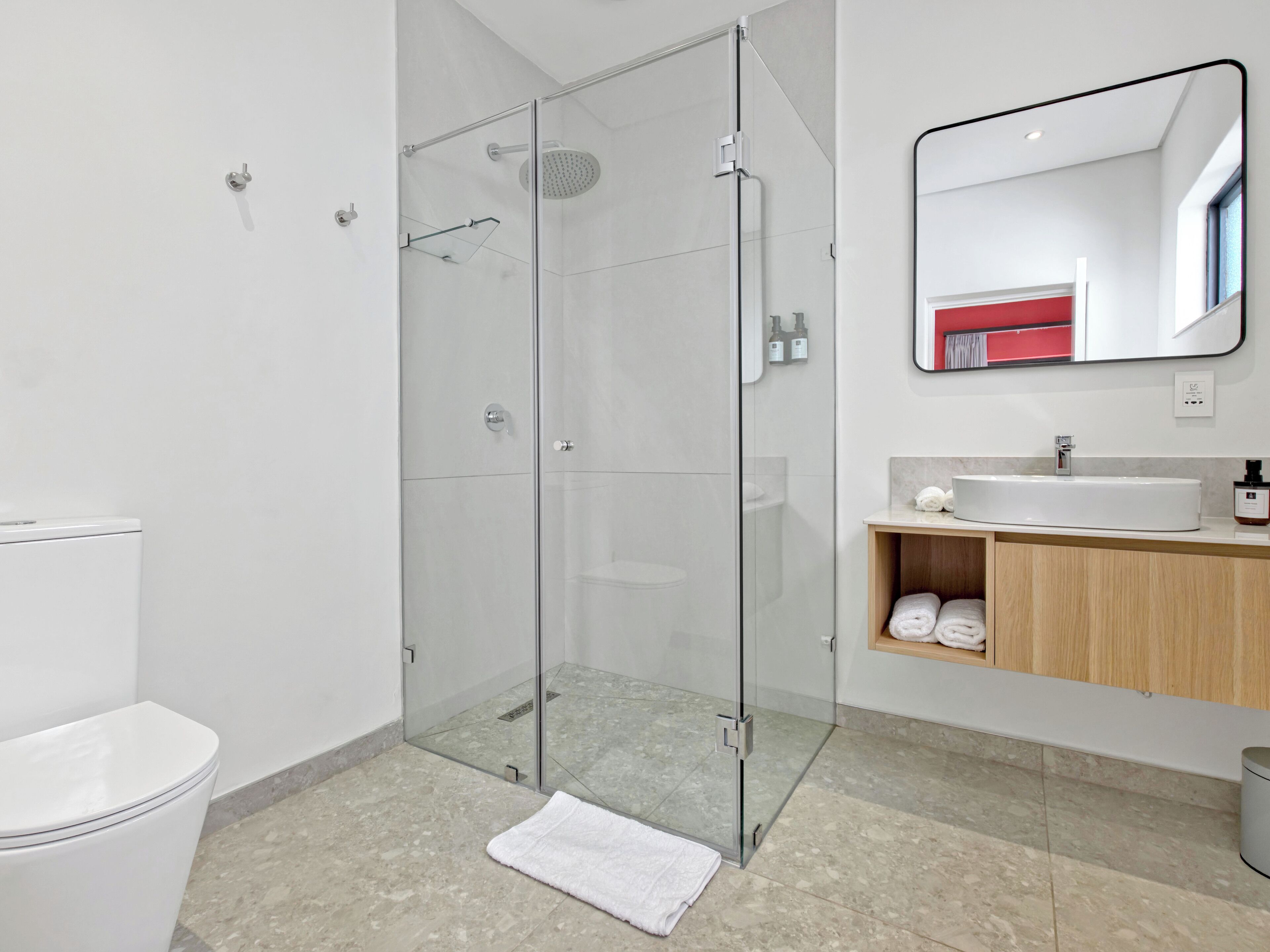 A modern bathroom with a glass-enclosed shower, a white toilet, a sink with a wooden vanity, and a mirror above the sink.