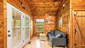 L’intérieur d’un chalet en bois, avec un canapé gris, une petite table en bois et une porte dotée d’une poignée.