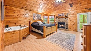 Une chambre située dans un chalet en rondins, avec un lit, une cheminée, un plafond en bois et une fenêtre avec des rideaux.