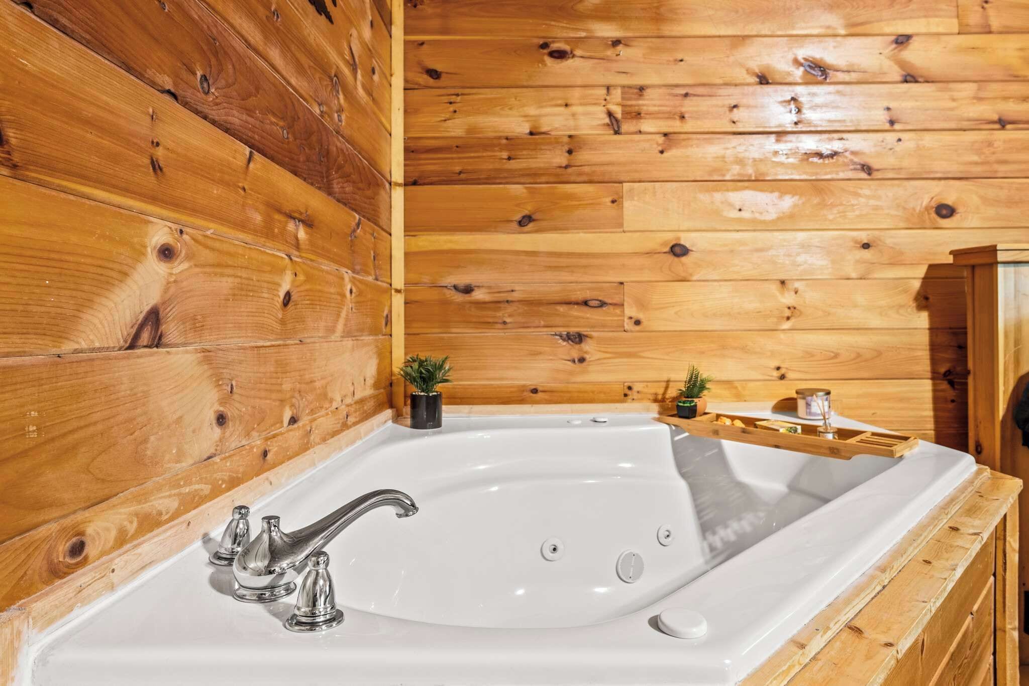 A wooden cabin interior with a large bathtub, wooden walls, and a small potted plant.