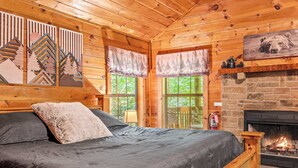 L’intérieur d’un chalet en bois, avec un lit, une cheminée et une fenêtre donnant sur la forêt.