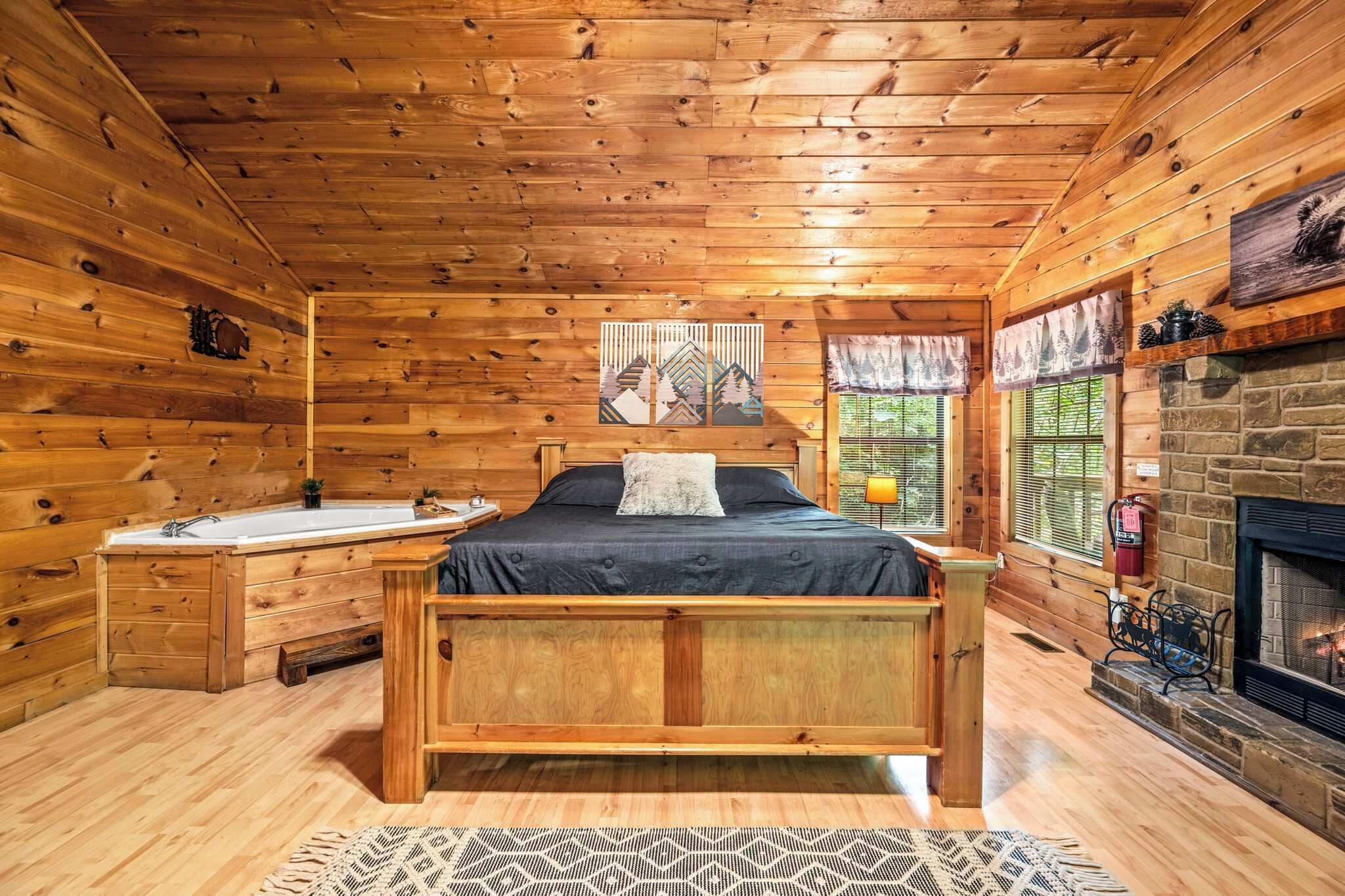 A log cabin bedroom with a bed, a fireplace, a window with curtains, and a wooden floor.
