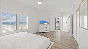 A bedroom with a bed, a TV, a dresser, and a view of the beach through the windows. - Palm Beach 41A by Liquid Life (Orange Beach)
