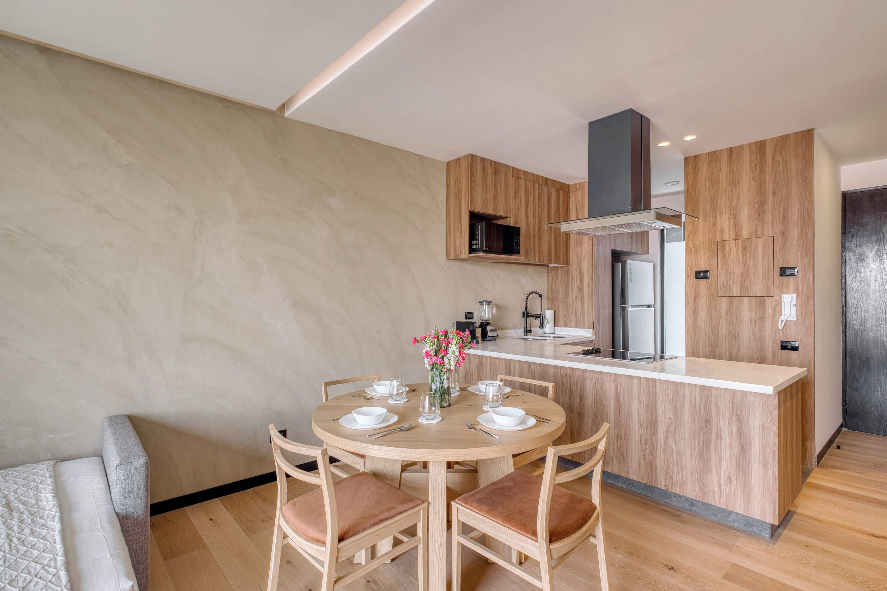 A modern kitchen with wooden cabinetry, a central island, and a dining area with chairs and a table.