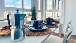 Una mesa de desayuno con una cafetera, tazas y pasteles, en un balcón con vistas a la ciudad.