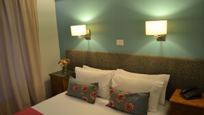 A hotel room with a bed, two wall-mounted lamps, a nightstand with a phone, and a vase with flowers. - Individual room in the Heart of the town (El Calafate)