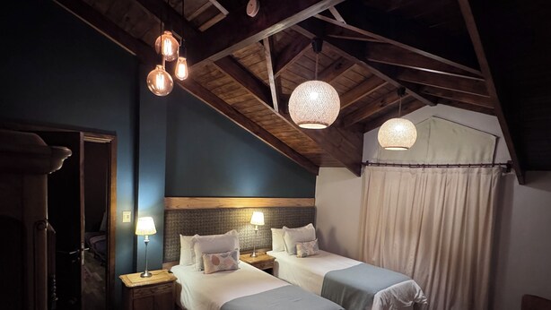 Una habitación acogedora con dos camas, vigas de madera y lámparas colgantes.
