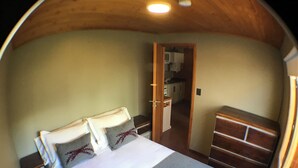 Un dormitorio con cama, cómoda y puerta que da a una cocina.