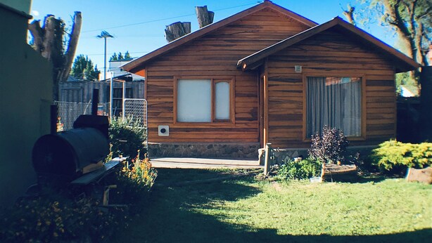 Una cabaña de madera con base de piedra, un pequeño porche y un jardín bien cuidado.