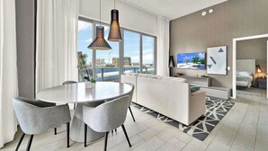 Ein modernes Hotelzimmer mit Essbereich, einer Couch, einem Fernseher und Blick auf die Stadt.