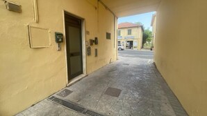 A narrow alleyway with a yellow building, a door, and a small vent on the wall.
