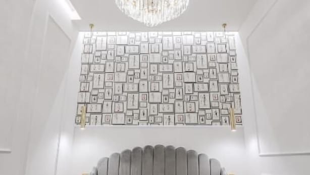 A modern hotel room with a large bed, a chandelier, and a wall decorated with framed pictures.