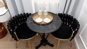 A round table with a marble top, two black velvet chairs with gold accents, and a tray with two wine glasses and two white cups.
