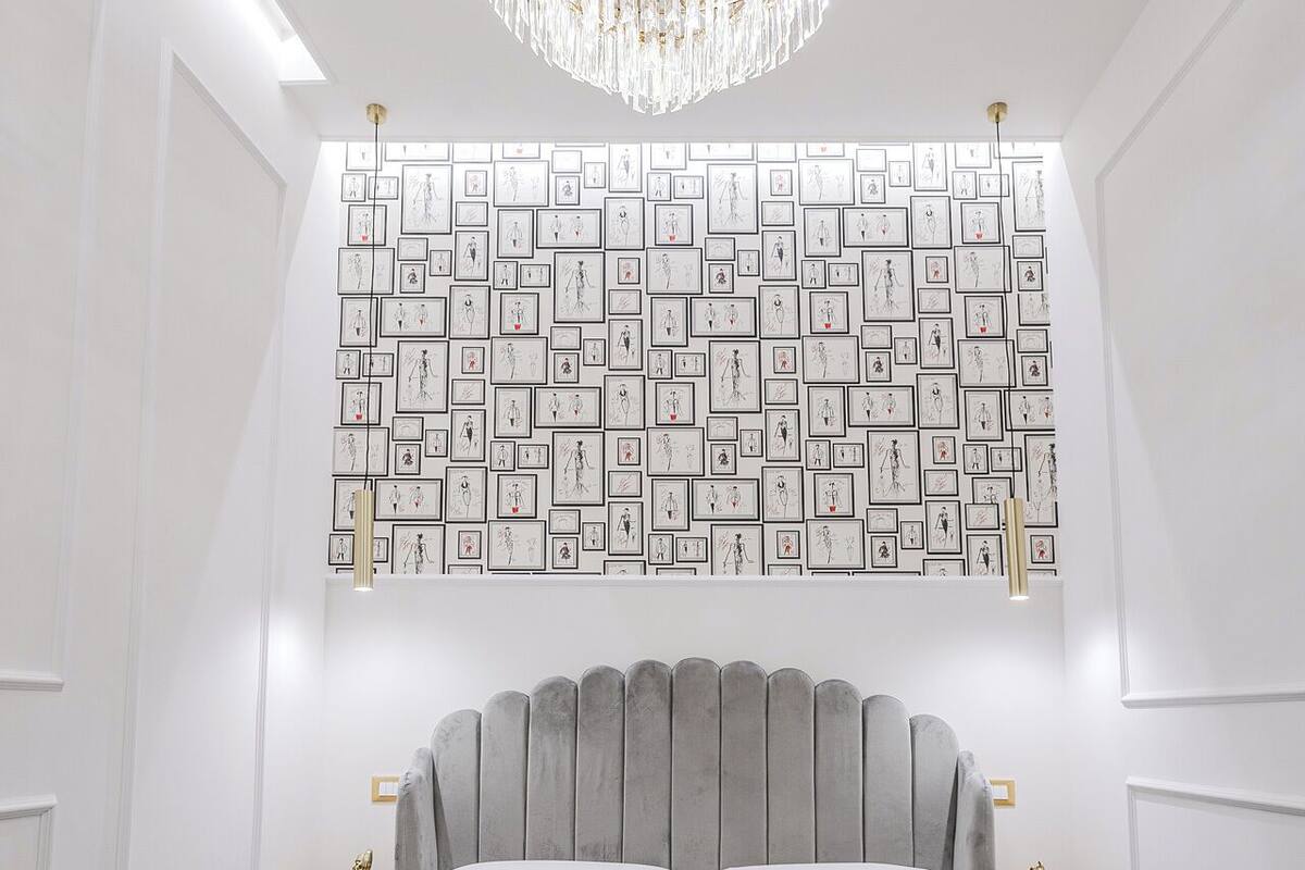 Ein modernes Schlafzimmer mit einem großen Bett, einer Chandelierleuchtre und einer Wand voller gerahmter Skizzen.
