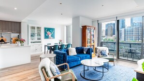 En moderne stue med en blå sofa, spiseplads og udsigt til byens skyline gennem store vinduer.