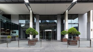 En moderne bygningseingang med en drejebeslag, glasfacade og plantede træer.
