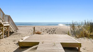 Ein hölzerner Promenadenweg führt zum Meer, mit einer Holztreppe links und einem Geländer rechts.