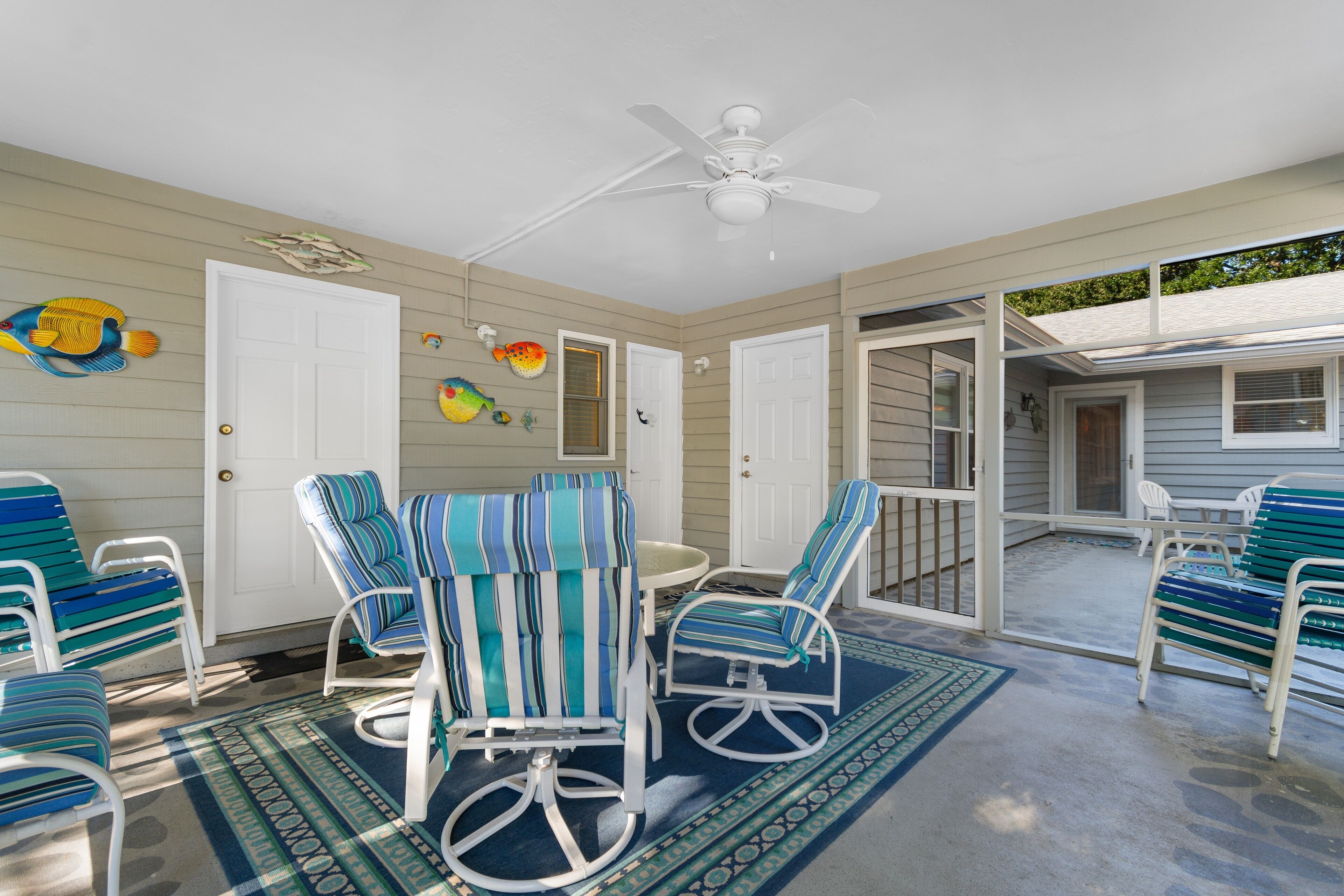 A covered patio with striped chairs and a table, a ceiling fan, and decorative fish wall art.