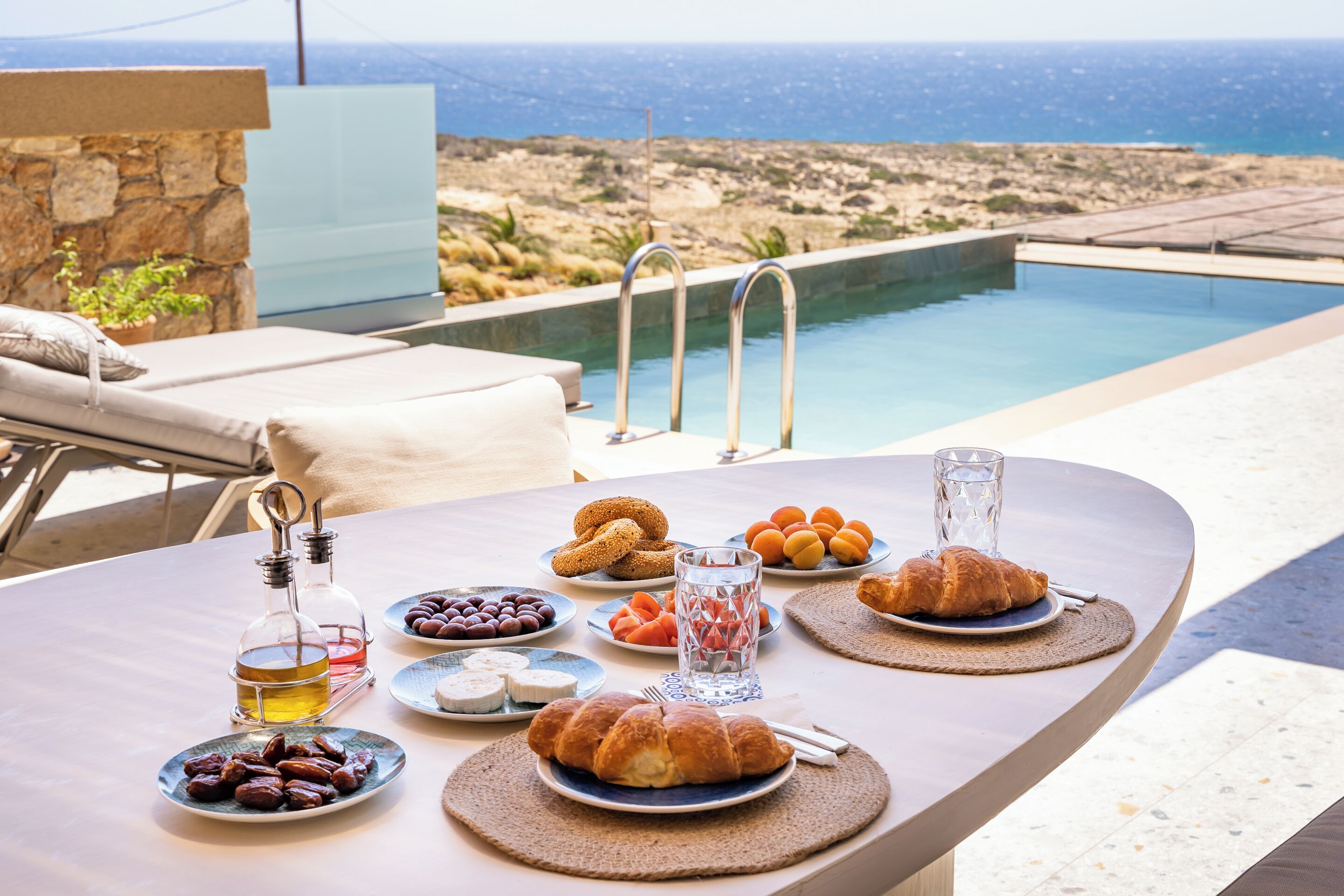 Mesa com comida e bebidas, com vista para uma piscina e uma paisagem deslumbrante.