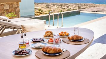 Mesa com comida e bebidas, com vista para uma piscina e uma paisagem deslumbrante.