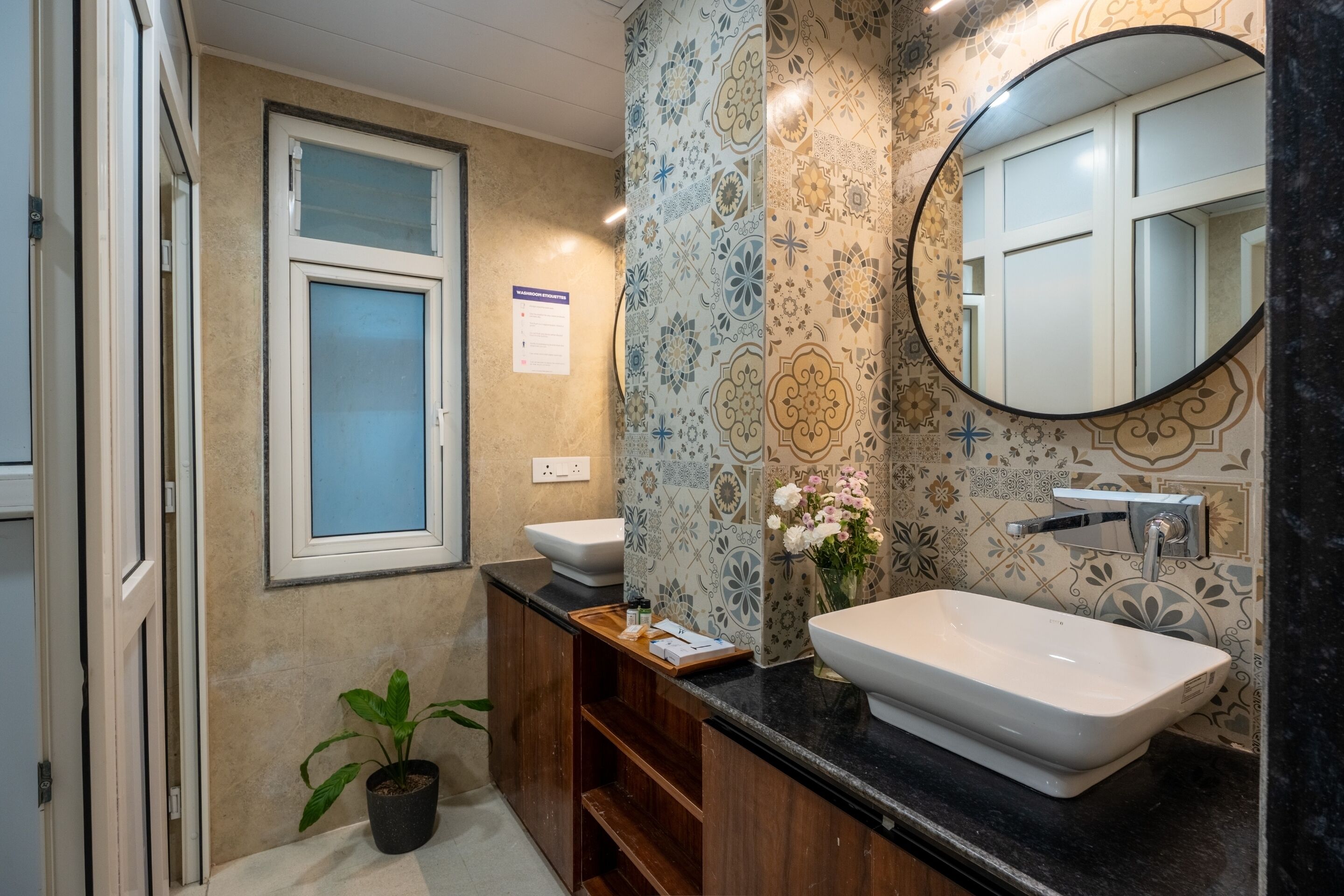 A bathroom with a large window, two sinks, a mirror, and a potted plant.
