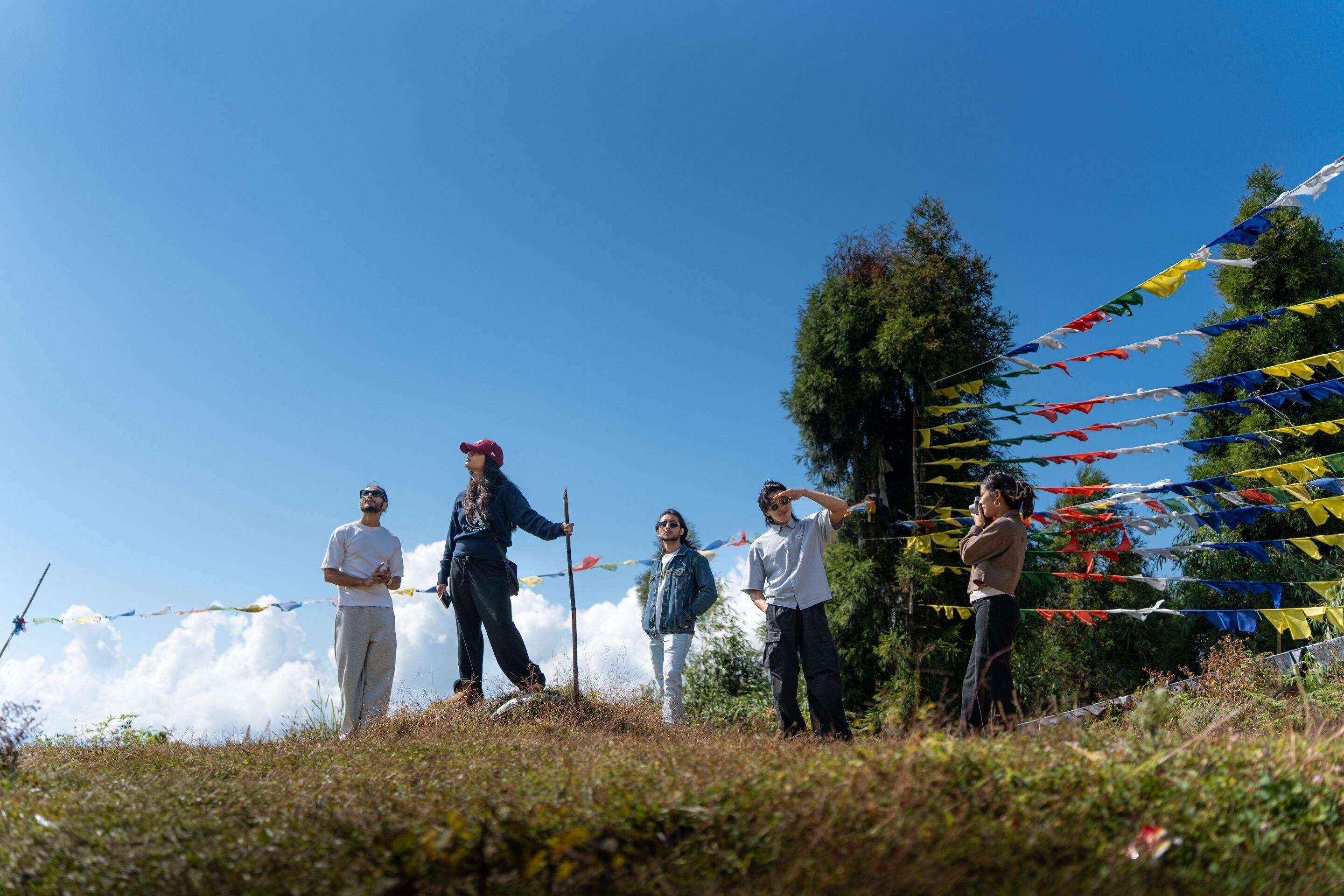 A group of people standing on a grassy hill with colorful flags in the background.