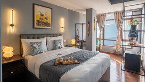 Ein modernes Schlafzimmer mit einem großen Bett, Nachttischlampen, einem Gemälde und Bergblick durch das Fenster.