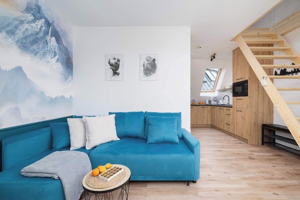 A bright living area with a turquoise sofa, white walls, and wooden accents. The setup feels cozy and inviting, ideal for relaxation.