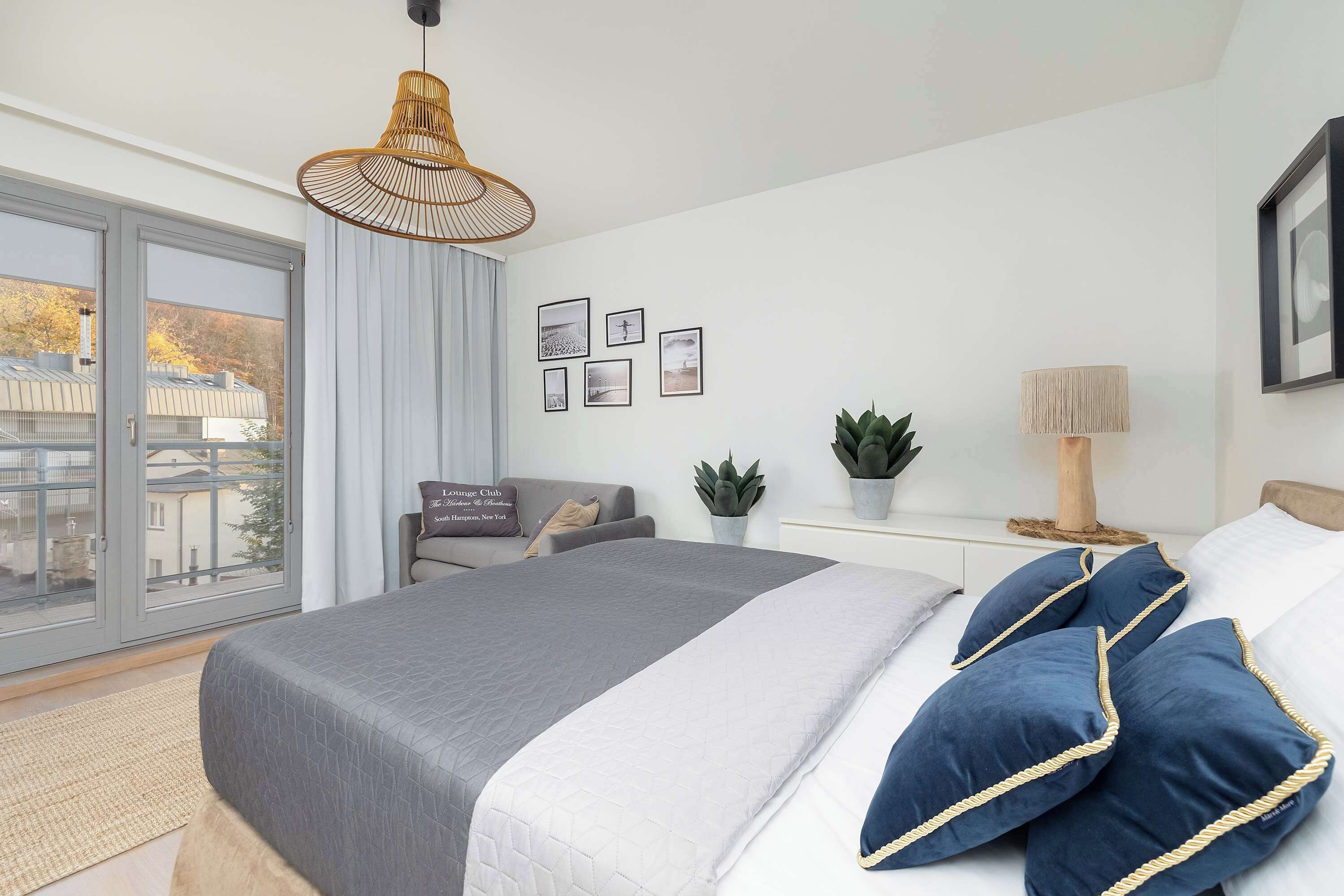 Un dormitorio moderno con una cama grande, vistas a través de ventanales del suelo al techo, una lámpara colgante y una mesita de noche con lámpara.