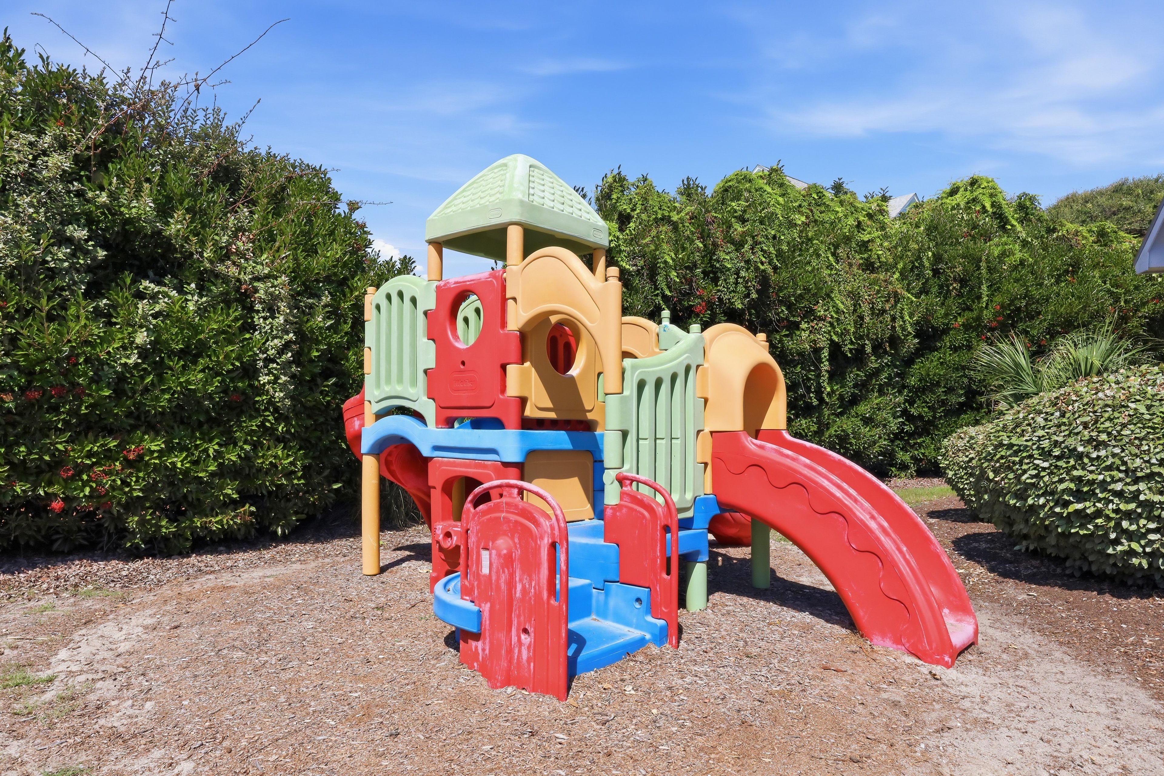 A children's play structure with a slide and climbing elements, surrounded by dense shrubbery.