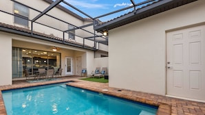 A swimming pool with a tiled deck, a covered patio area with seating, and a door to the right. - NEW Paradise Splash Villa! (Kissimmee)