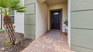 A building entrance with a palm tree, a dark door, and a small potted plant. - NEW Paradise Splash Villa! (Kissimmee)
