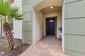 A building entrance with a palm tree, a dark door, and a small potted plant. - NEW Paradise Splash Villa! (Kissimmee)
