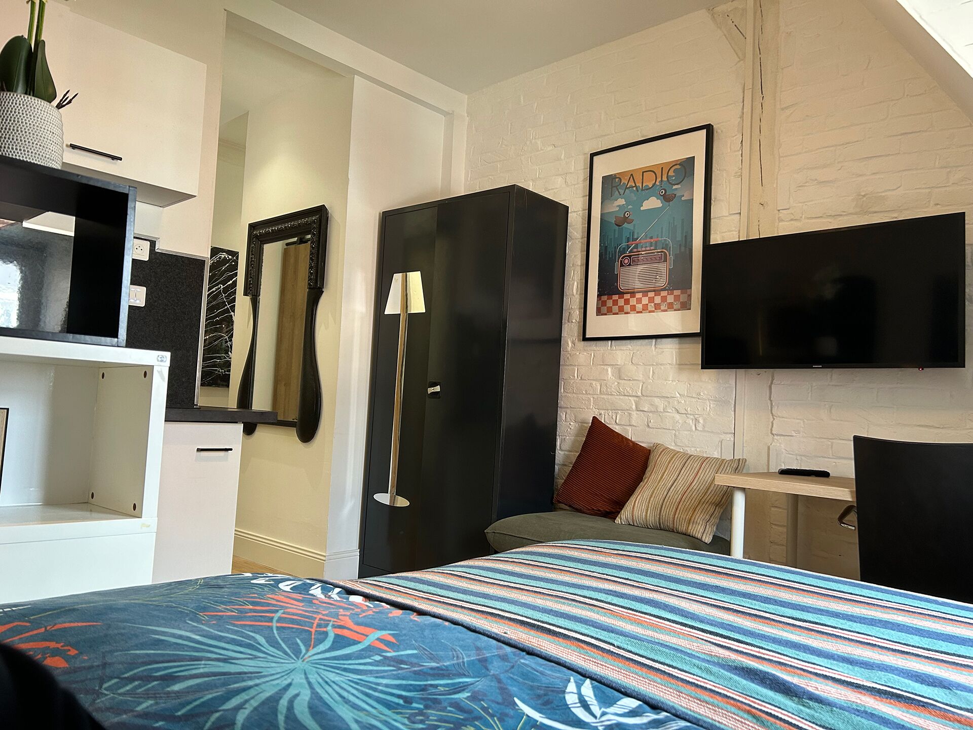 A bedroom with a bed, a TV, a wardrobe, and a mirror.
