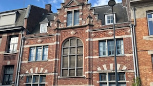Un bâtiment historique doté d’une fenêtre en arc en plein cintre remarquable, d’une façade en briques et de nombreuses fenêtres avec volets.