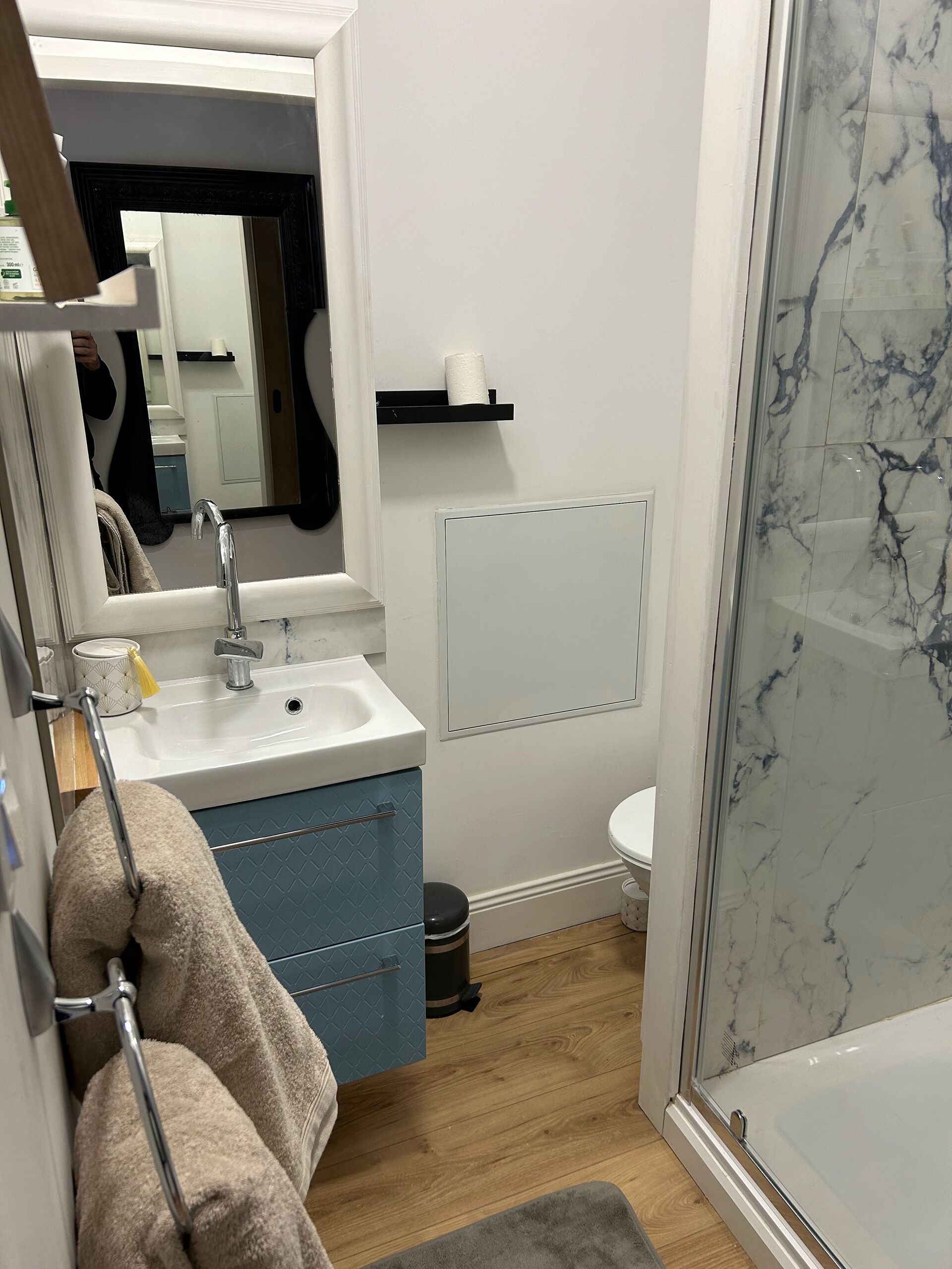 Ein Badezimmer mit einem weißen Waschbecken, blauen Schränken, einem Spiegel, einer Toilette und einer Duschkabine aus Glas.