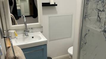 Ein Badezimmer mit einem weißen Waschbecken, blauen Schränken, einem Spiegel, einer Toilette und einer Duschkabine aus Glas.
