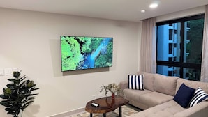 Ett modernt vardagsrum med en beige soffa, ett soffbord, en stor platt-TV och en krukväxt.