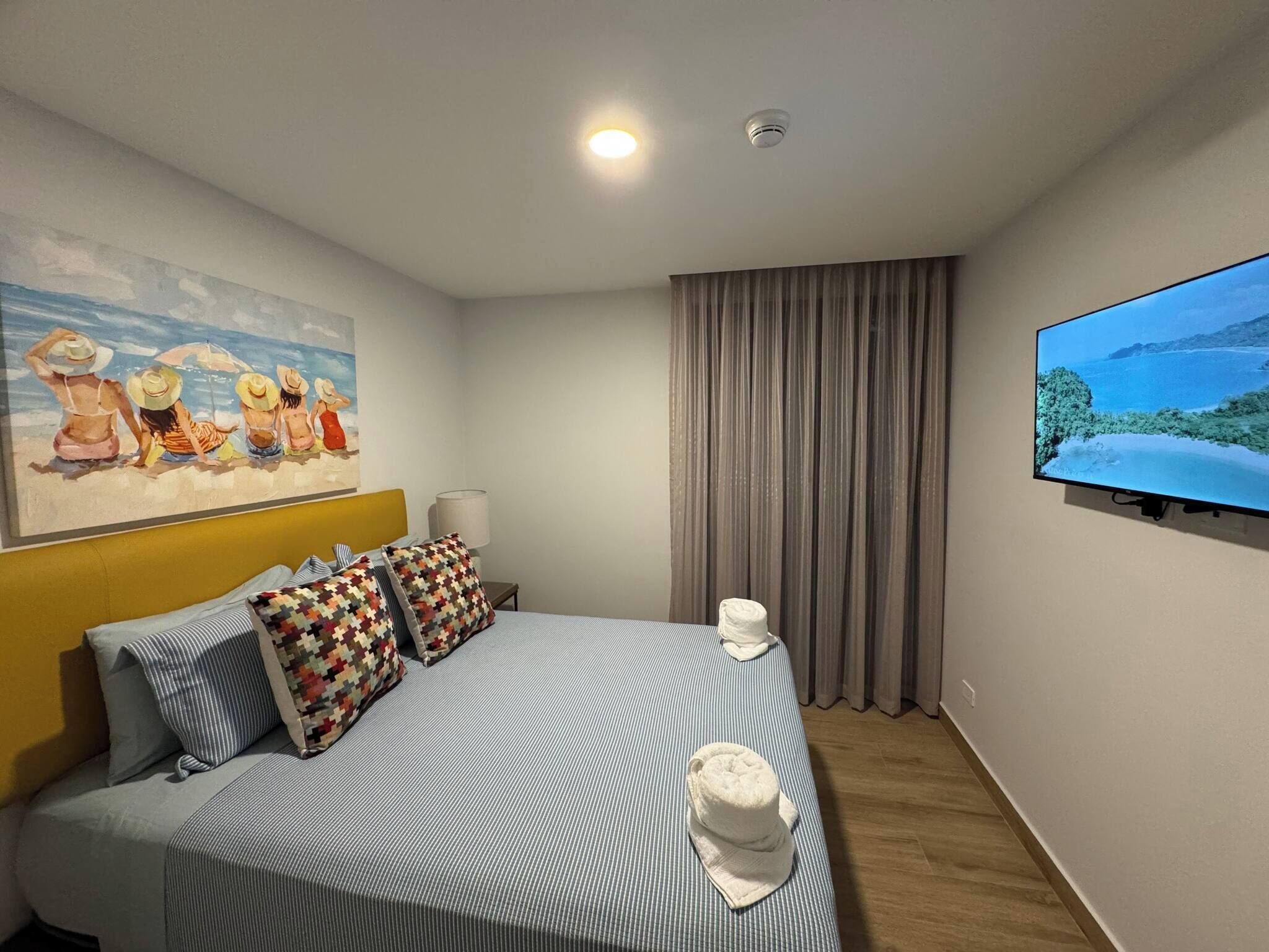 Een hotelkamer met een bed, een schilderij, een televisie en een raam met gordijnen.