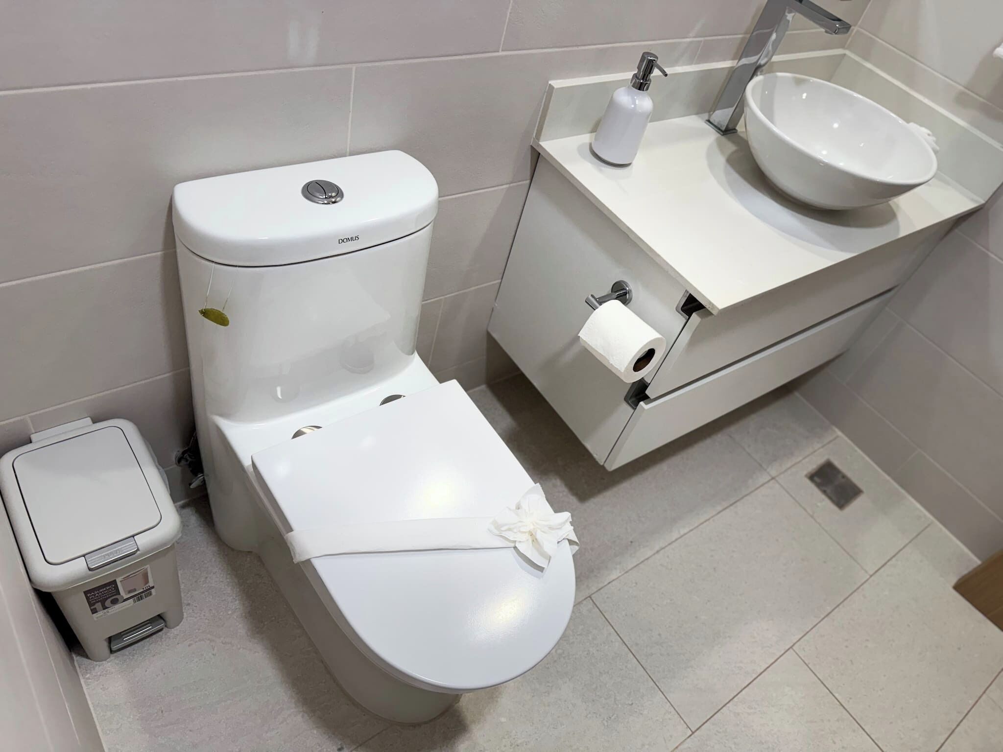 Et moderne badeværelse med et hvidt toilet, en vask og en skraldespand.
