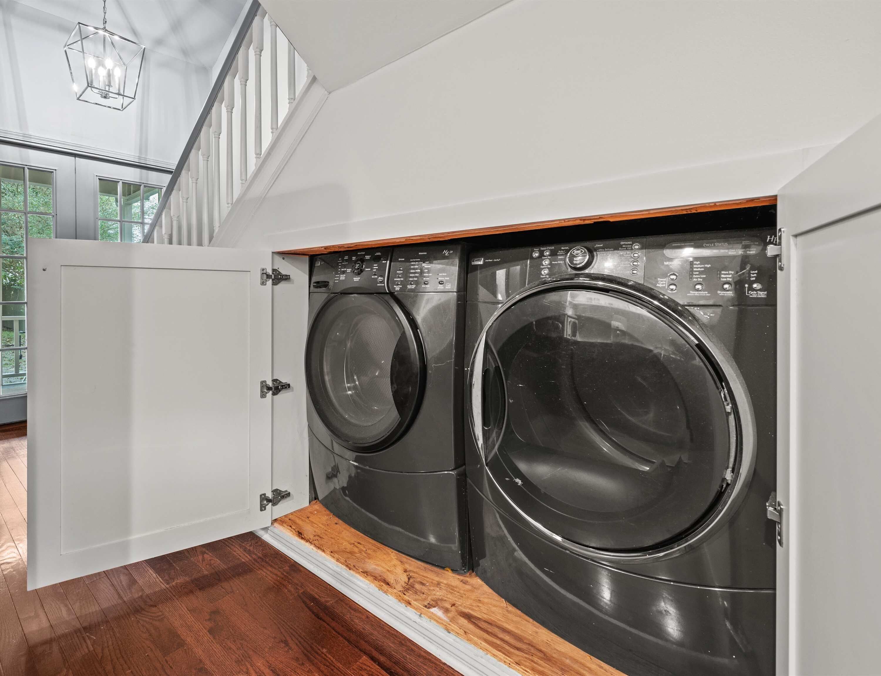 A modern laundry room with two front-loading washing machines, wooden flooring, and a white door.