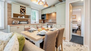 Et moderne køkken med indbyggede hårde hvidevarer, et spiseområde med et bord dækket til to, og et hyggeligt soveværelse, der kan anes gennem en åben dør.