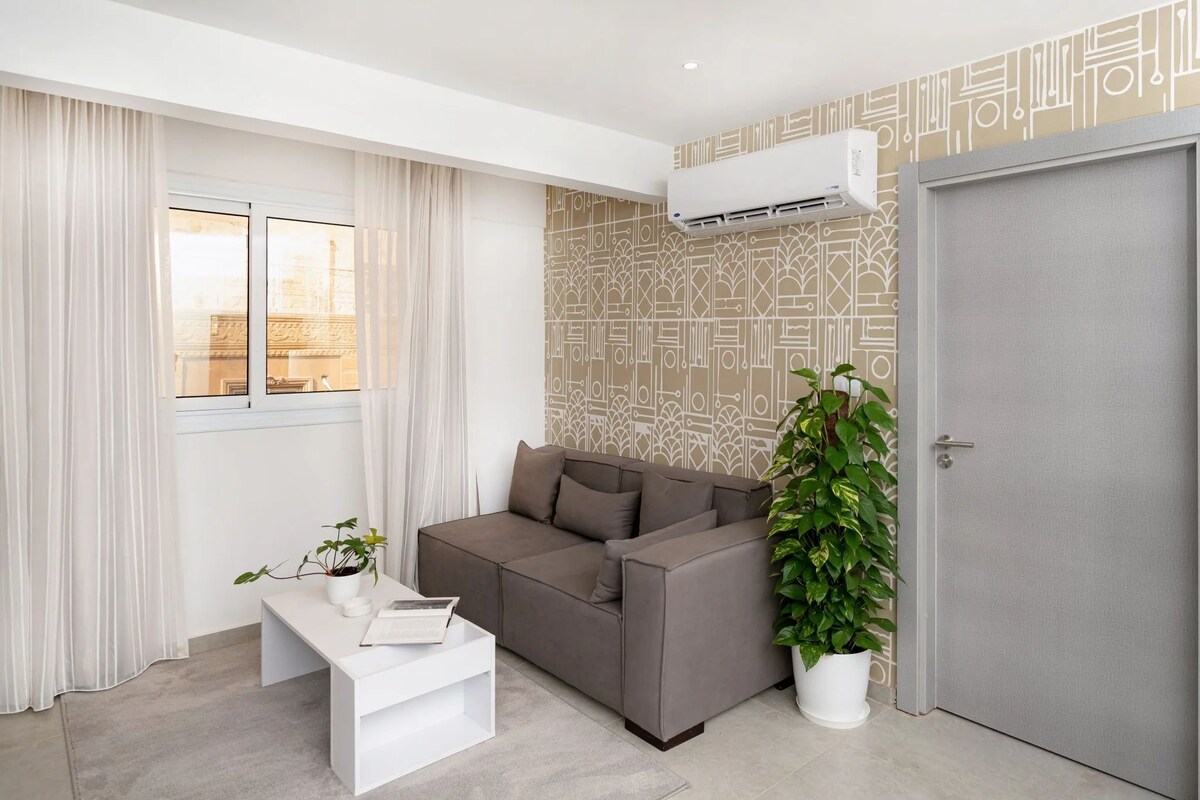Ein modernes Wohnzimmer mit einem grauen Sofa, einem weißen Couchtisch, einer Topfpflanze und einer Wand mit Muster.