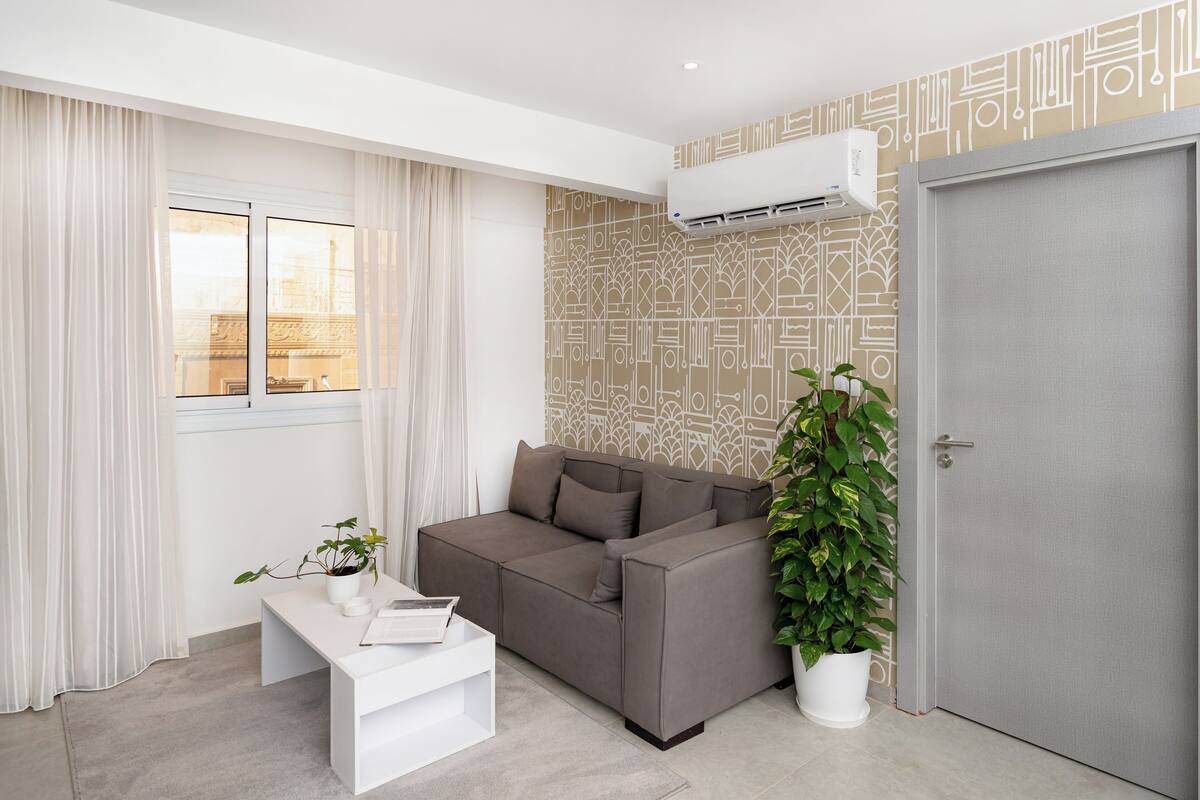 A modern living room with a grey sofa, a white coffee table, a potted plant, and a patterned wall.