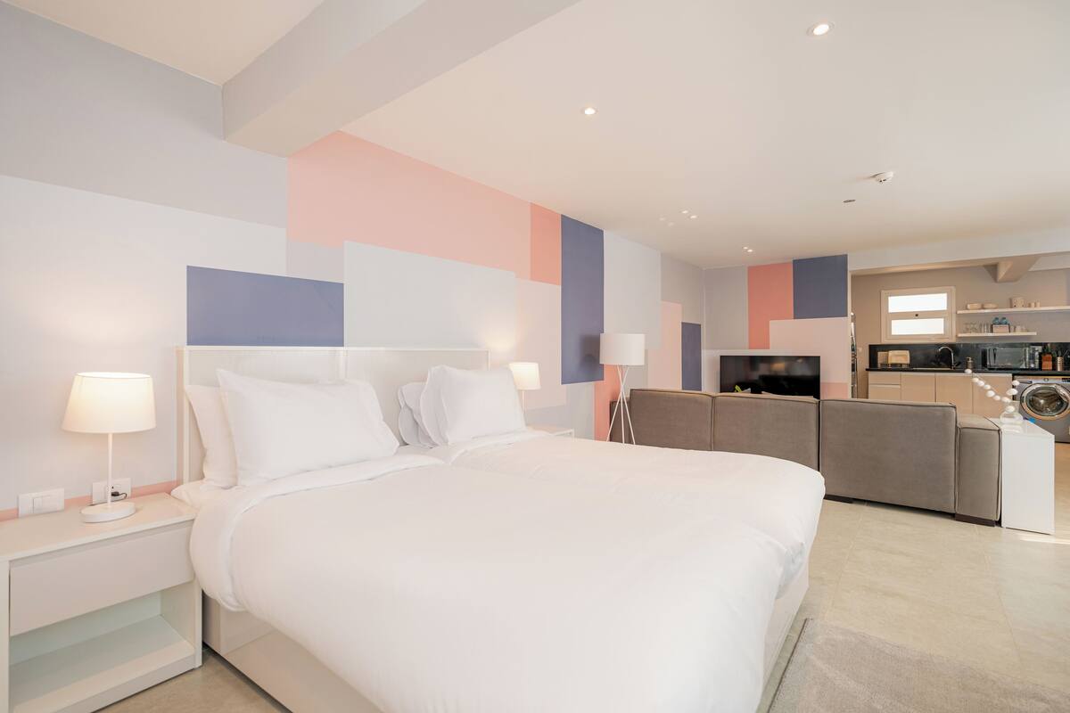 A modern hotel room with a large bed, bedside tables, a desk, and a kitchenette.