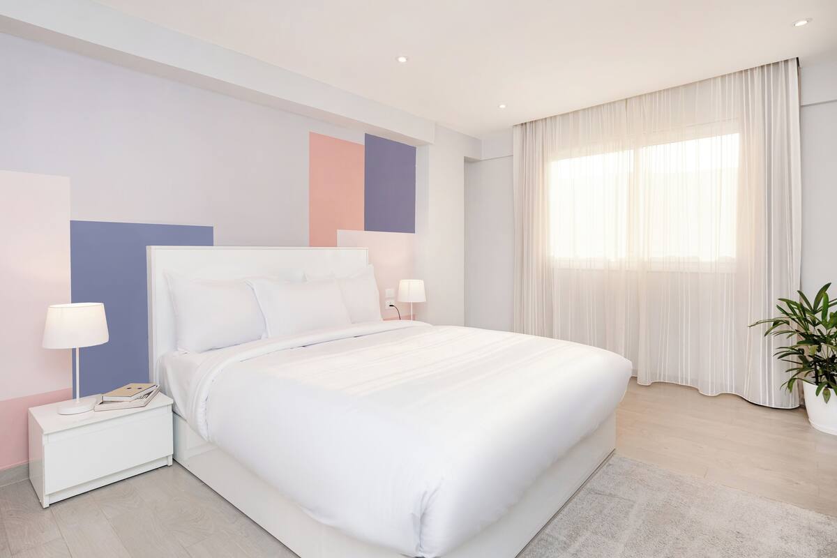 A modern bedroom with a large bed, bedside tables, a lamp, and a potted plant.