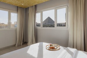 Ein Hotelzimmer mit Bett, einem Tablett mit Speisen und Blick auf eine Pyramide.